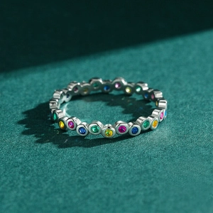 Macro shot of silver ring with colorful round-cut rainbow stones on dark green surface