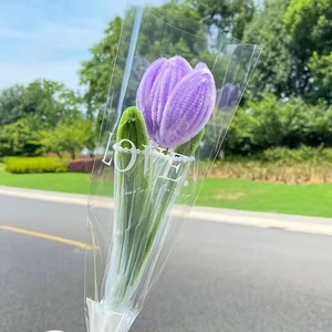 Single purple handmade plush tulip in LOVE packaging held outdoors with park background
