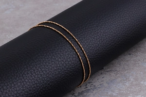 Macro shot of two delicate gold chain necklaces displayed on black leather texture