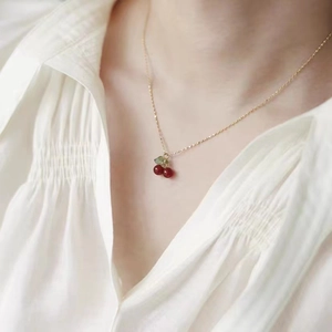 Chic cherry pendant necklace with red beads and golden chain on white textured shirt