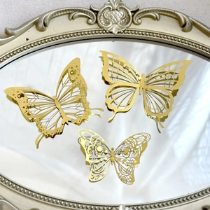 Detail showing three golden hollow-out paper butterflies on a vintage carved mirror