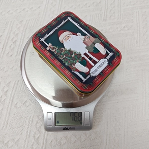 Tin Christmas candy box weighing 76.8g on a digital scale for package detail
