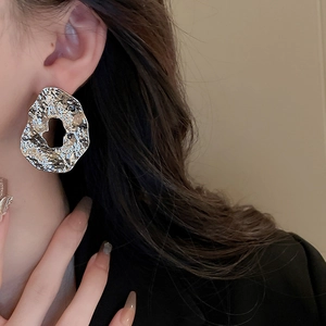 Close-up of model wearing textured silver metallic irregular hollow round earrings