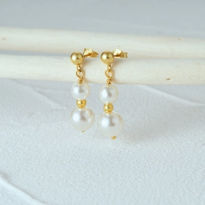 Macro shot of 925 silver double pearl drop earrings with golden metal studs and minimal detail