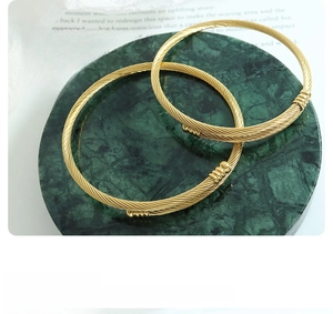 Close-up of two gold-plated twisted cable open bangles on green marble display
