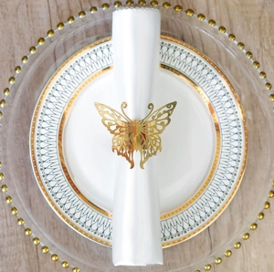 Close-up of a golden hollow butterfly napkin ring on a white plate with wood background