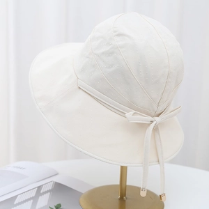 Elegant beige wide-brim sun hat with polka dot texture and bow detail on gold stand