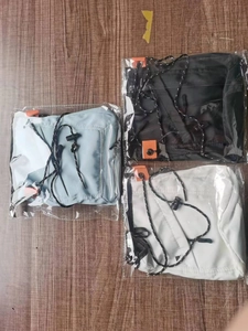Three nylon crossbody bags in black, white, and light blue on a wooden surface