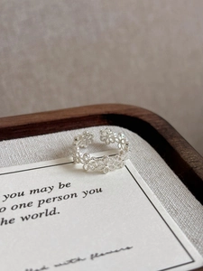 Detailed close-up of hollow flower silver ring with adjustable open band on card