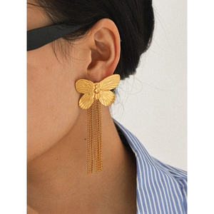 Close-up of gold butterfly tassel earrings with hanging metal chains on a model