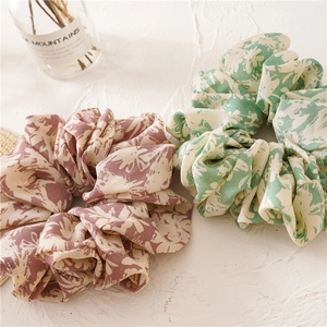 Oversized floral print scrunchies in pink and green fabric on a textured white surface
