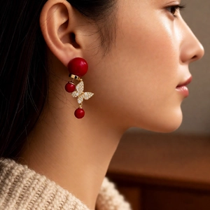 Gros plan d'une femme portant des boucles d'oreilles papillon dorées 18k et perles rouges