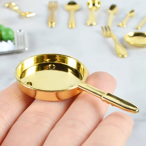 Miniature golden alloy frying pan and cutlery set shown between fingertips for scale