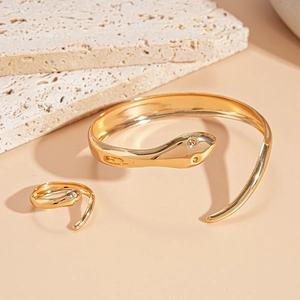 Dettaglio del set bracciale e anello a forma di serpente dorato su fondo in pietra