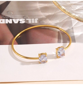 Close-up of a gold stainless steel cuff bracelet with two square-cut zirconia stones