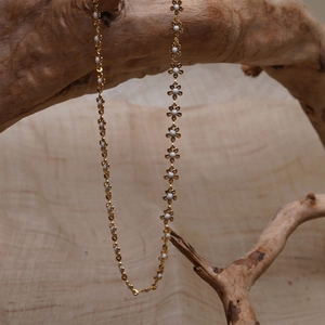 Elegant gold necklace with white enamel flower charms hanging on a natural wooden branch