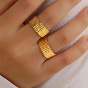 Detail view of wide gold titanium rings with vertical stripe texture on model's hand