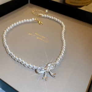Detailed view of pearl necklace featuring a sparkling rhinestone bow pendant and gold clasp