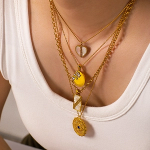 Layered gold necklaces with shell heart and devil eye charms worn by a female model