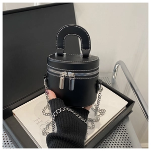 Détail d'un sac à main cylindrique noir avec surpiqûres blanches et bandoulière chaîne