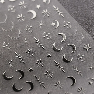 Metallic silver embossed nail stickers with tribal sun and moon patterns on a dark surface