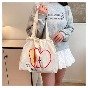 Close-up of a large beige nylon shoulder bag with a colorful apple print and drawstring