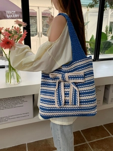 Detail of blue and white striped knit tote bag with a large decorative bow and thick texture