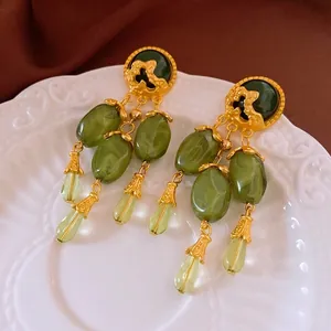 Vintage gold tassel earrings with green beads on elegant silk fabric background