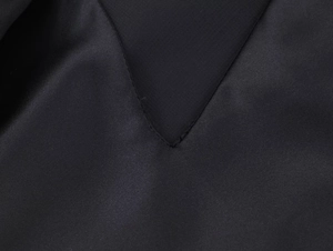 Detailed view of the V-neck seam and satin fabric texture on this black fashion dress