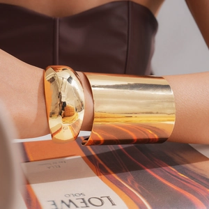 Nahaufnahme von minimalistischem goldfarbenem breitem Armreif und gewölbtem Armband-Set
