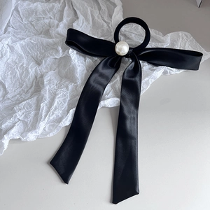 Close-up of black satin bow hair tie with an elegant pearl accent on beige surface
