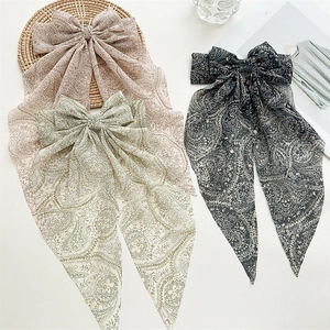 Three paisley print chiffon bow hair clips in pink green and black on a woven tray