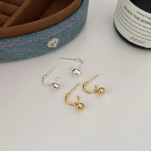 Set of gold and silver J-hoop earrings with metal bead drops on a white surface