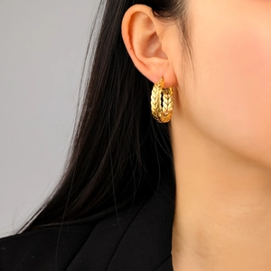 Golden wheat-patterned hoop earrings in stainless steel on a model with dark background