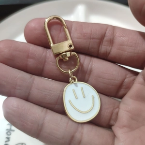 Close-up of golden alloy keychain with white enamel smiley face pendant held in hand