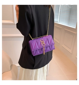 Detail of purple crossbody bag with geometric quilting and golden tassel on chain strap