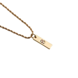 Detail of gold necklace featuring a rectangular pendant with colorful zircon letter B inlay