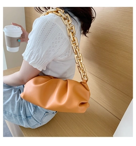 Detail of orange cloud pouch with chunky gold chain strap and pleated faux leather design