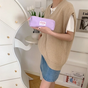 Purple canvas pouch with top zipper and white label detail held in a cozy home setting