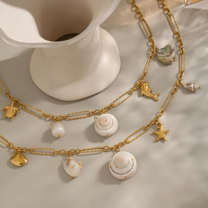 Collier double couche doré avec pendentifs tortue et dauphin sur un vase blanc