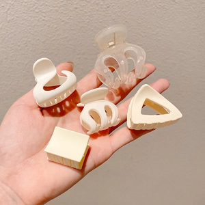Five assorted matte resin hair claws in geometric shapes held against a neutral wall