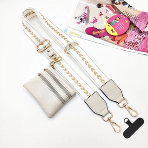Detail of white embroidered crossbody strap with gold accents and matching mini pouch