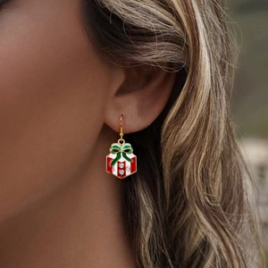 Golden Christmas gift box earrings with red stripes and green bow on a female model