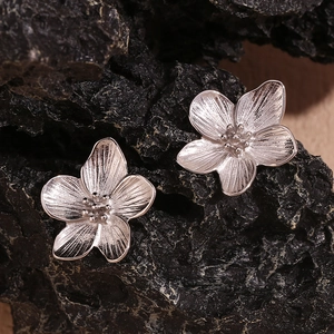 Macro shot of silver cherry blossom stud earrings on a dark volcanic stone background