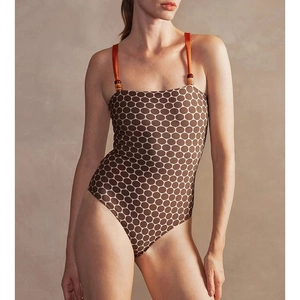 Close-up of brown polka dot swimsuit with orange beaded straps against a textured wall