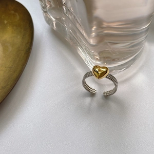 Detail of a two-tone twisted silver ring featuring a golden 3D heart on a white background