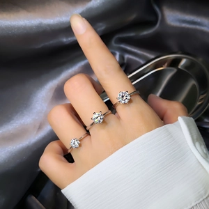 Three silver six-prong moissanite rings on model hands with silk background