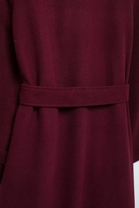 Détail du manteau en laine bordeaux montrant la texture du tissu et la ceinture assortie
