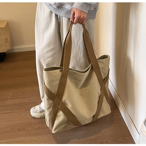 Detail of a large canvas tote bag featuring brown woven straps and reinforced construction