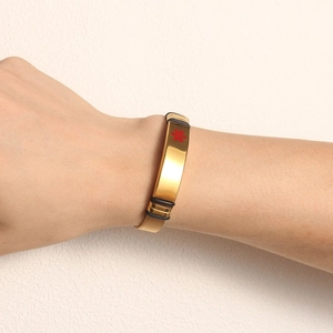 Detail of medical alert bracelet with gold mesh strap and red medical cross on gold plate
